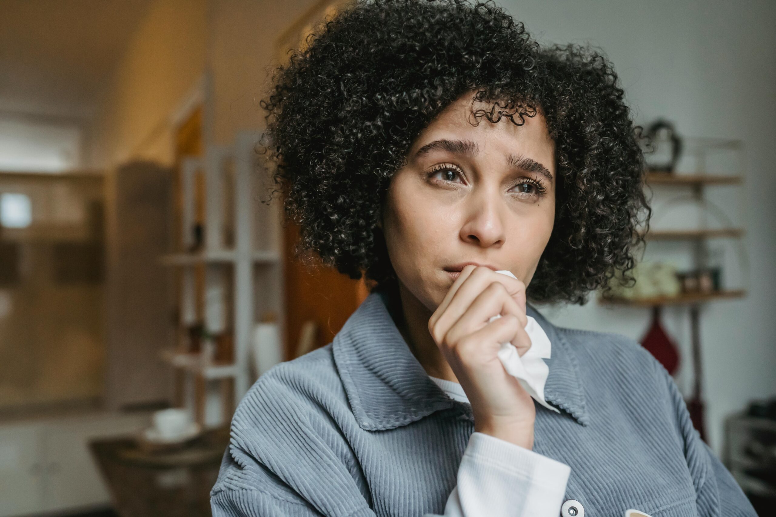 Portrait of a young woman with curly hair expressing sadness indoors.
